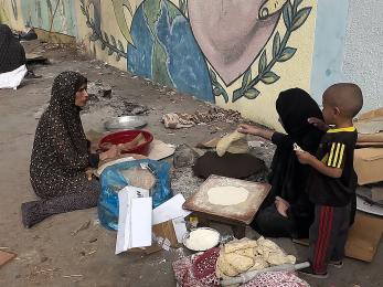 Two women in gaza prepare flatbread while a child looks on