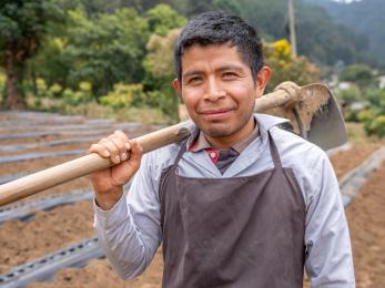 Guatemalan farmer stands smiling in field.