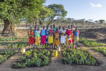 Kenyan community members standing as a group amidst agricultural crops.