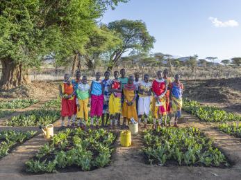 Kenyan community members standing as a group amidst agricultural crops.