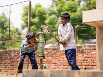 Two nepalese students work and use a water pump together.