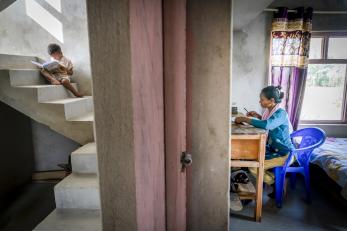 An person preparing to visit neighboring villages as their son reads books on the stairs of their home.