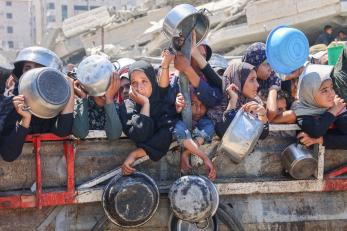 Palestinians holding empty pots and pans await a food delivery