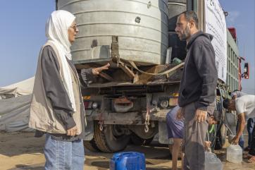 Palestinians, at a water tender, interact in discussion.