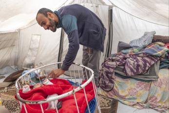 Palestinian father engages with child in bassinet. 