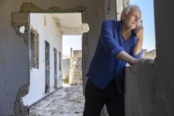 Syrian man standing in outdoor hallway, smiling.