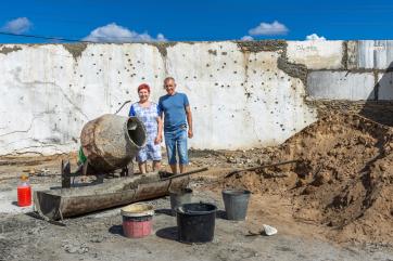 Farmers standing in front of a warehouse on their property that was damaged during russian occupation.