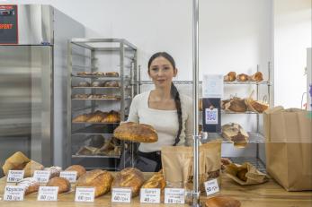 Ukrainian woman, a baker, stands in her bakery, behind loaves of bread.